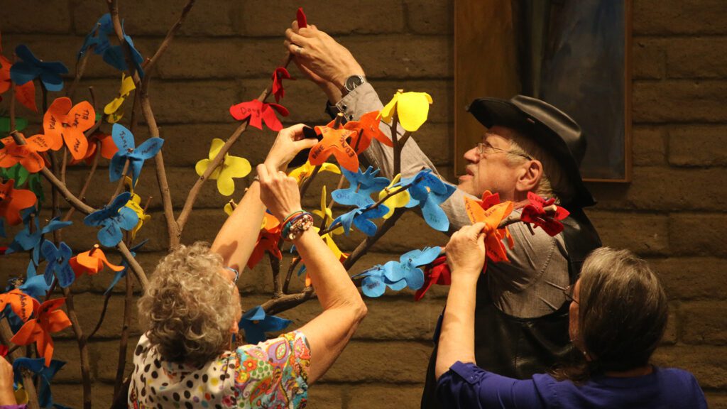 3 UUCP congregants affixing felt flowers with names and messages on them to branches in the sanctuary - Day of the Dead service
