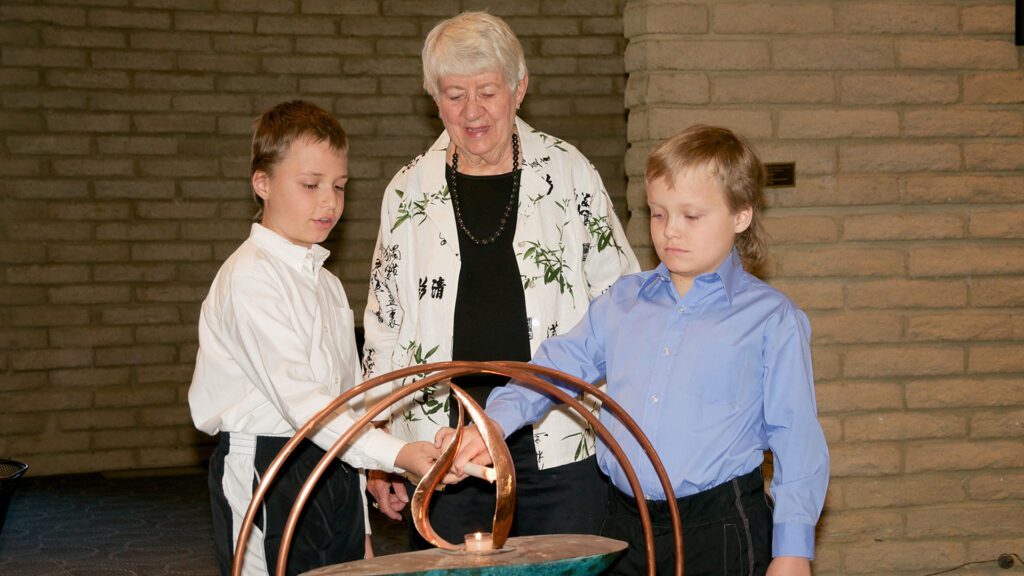 Young twin siblings lighting the UUCP chalice under the watchful eye of an adult
