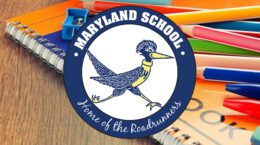 Spiral bound notebook and colored pencils on wooden desk overlaid with Maryland School logo