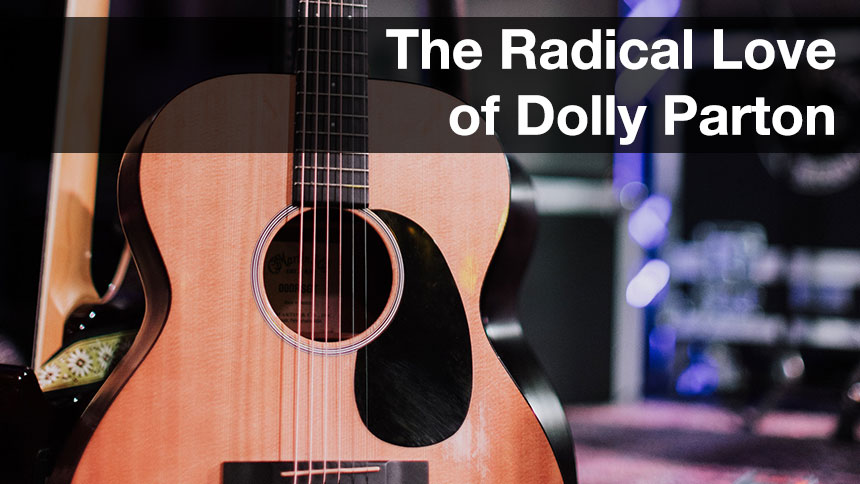 A guitar sitting on a guitar stand on stage with audio equipment in the background