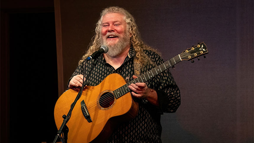 Joe Jencks at the microphone, with an acoustic guitar