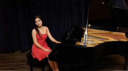 Taylisse Boissonneault sitting at a grand piano with a black backdrop.